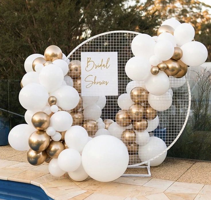 a bunch of white and gold balloons in front of a pool