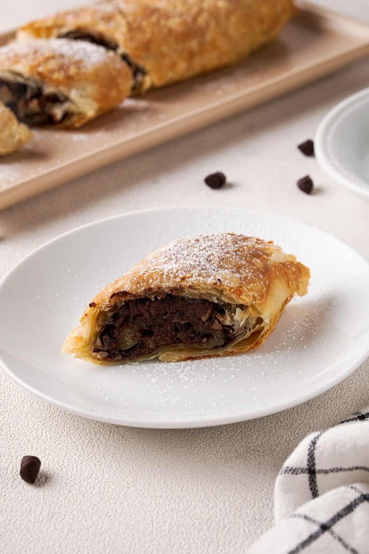 a pastry on a white plate with chocolate chips next to it and a wooden cutting board