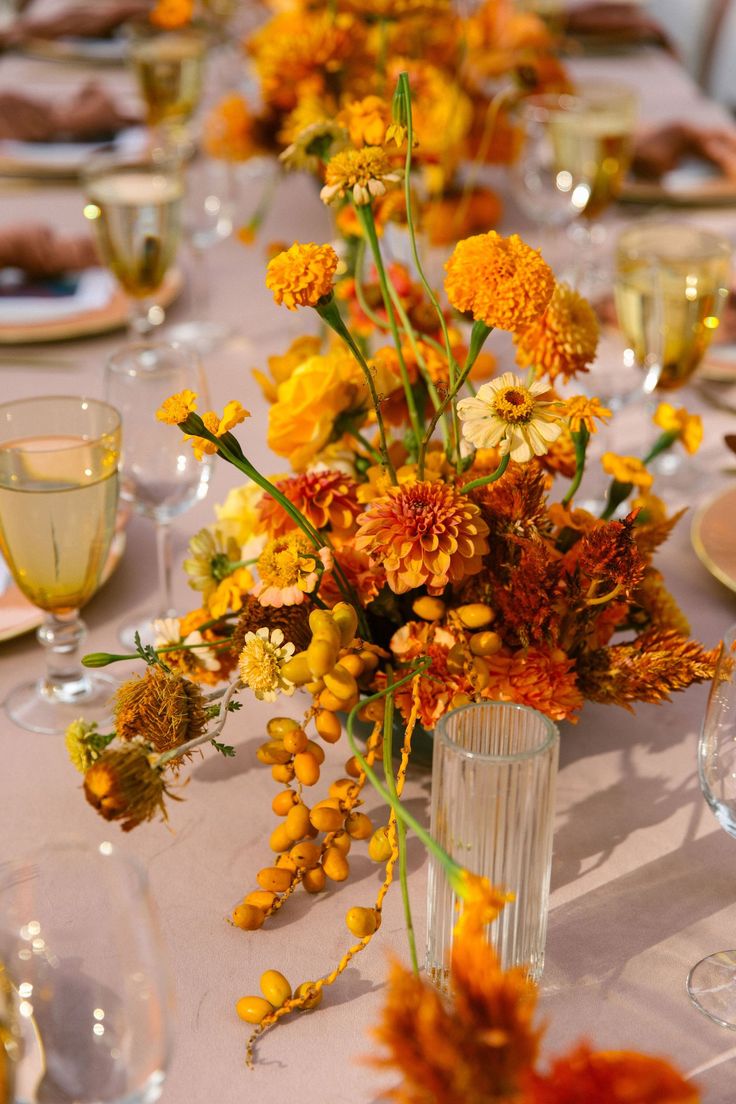 the table is set with orange and yellow flowers in tall vases on each side