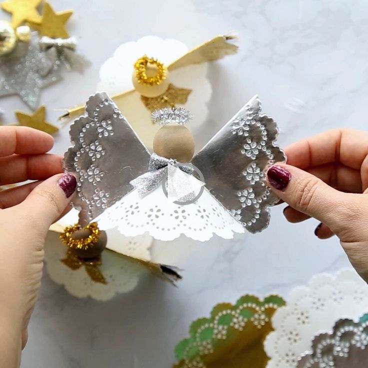 two hands are holding an origami angel with sequins and gold accents