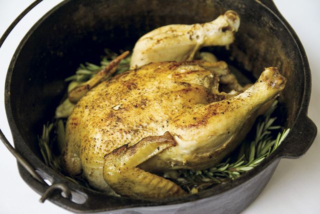 a whole chicken in a cast iron skillet with rosemary sprigs on the side