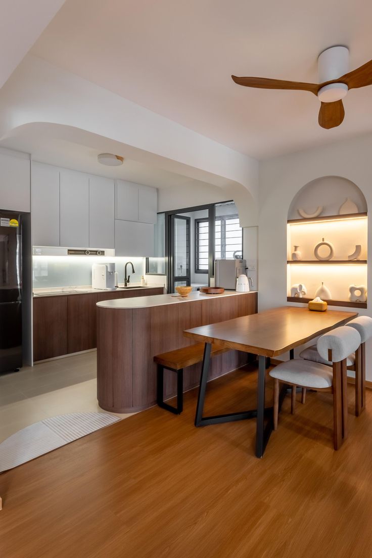 an open kitchen and dining room with wood flooring, white walls and ceiling fan