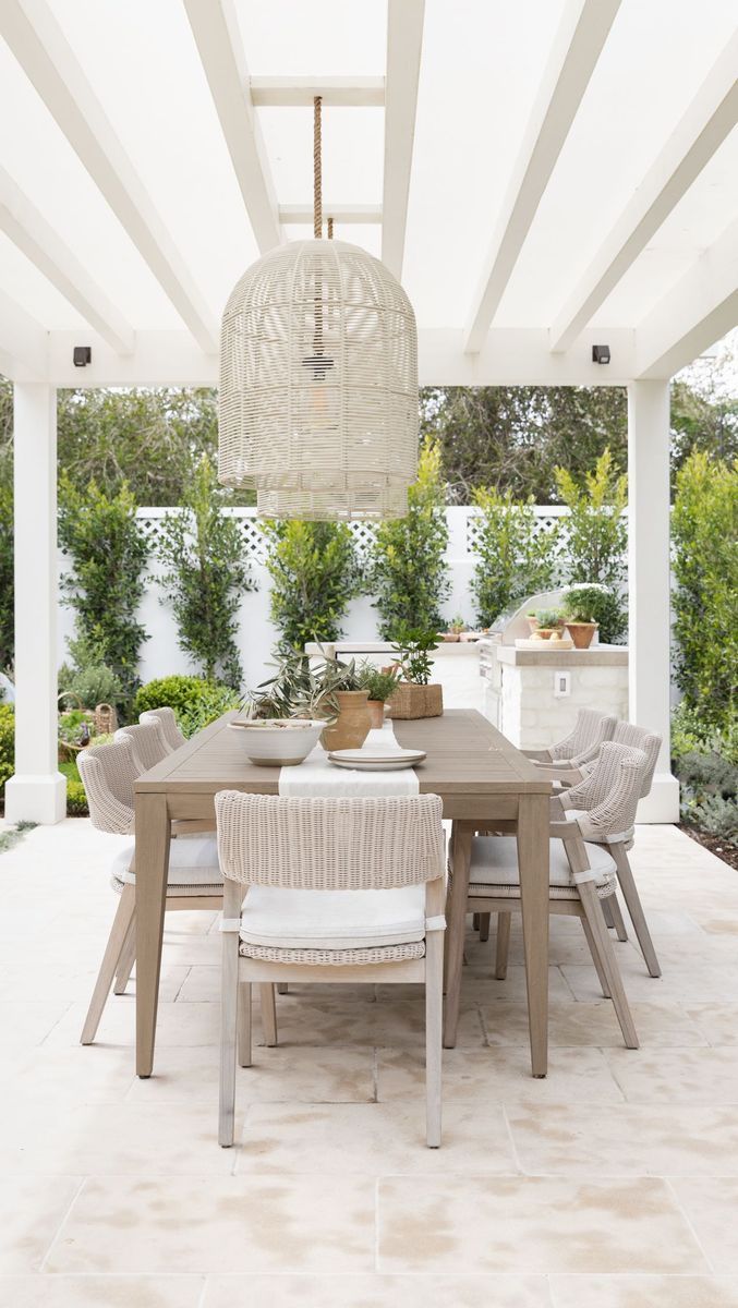 an outdoor dining table and chairs under a white pergolated roof