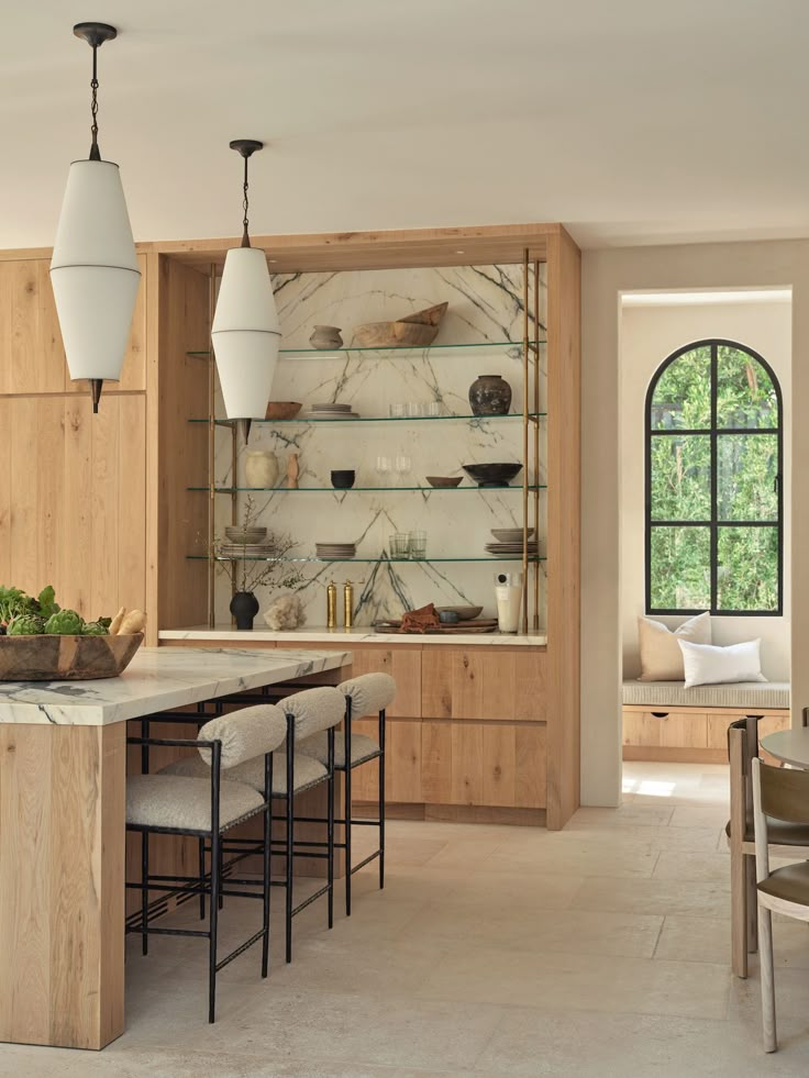 a kitchen with marble counter tops and wooden cabinets, along with hanging lights over the dining room table