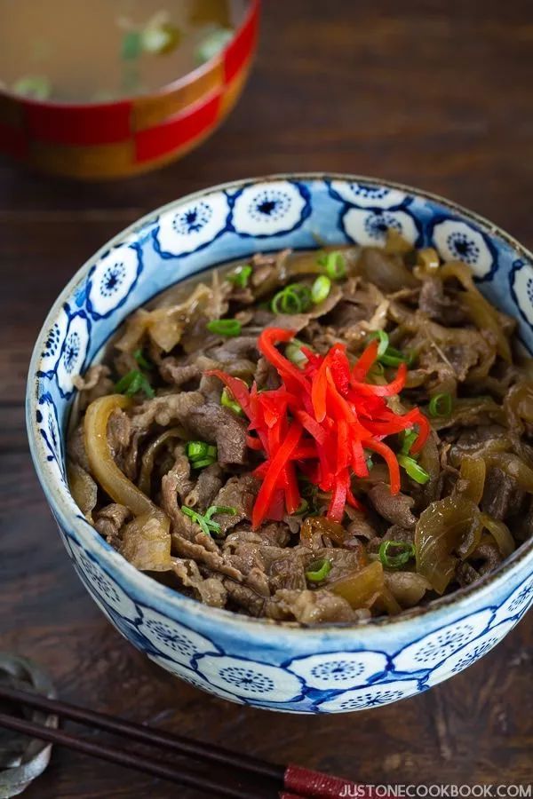 a blue and white bowl filled with food on top of a wooden table next to chopsticks