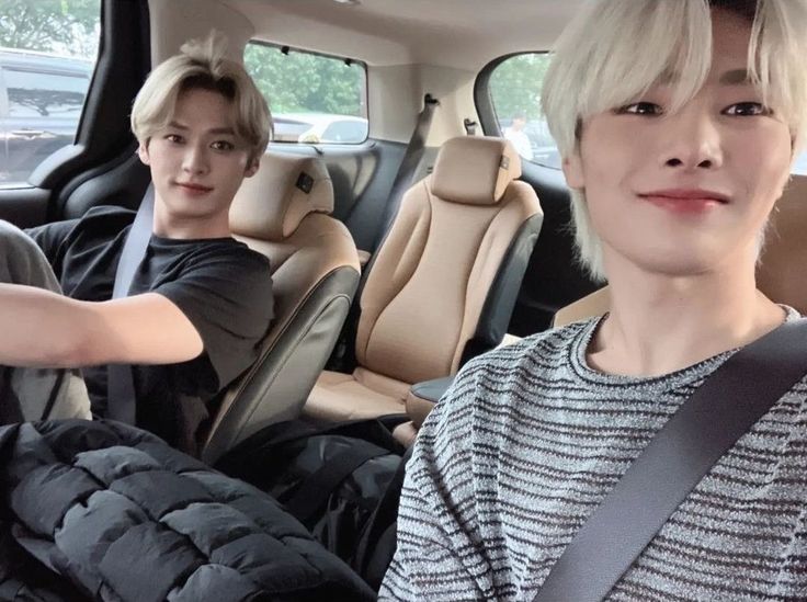 two young men sitting in the back seat of a car, one with blonde hair