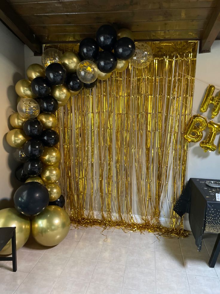 gold and black balloons are hanging from the ceiling in front of a party backdrop with streamers