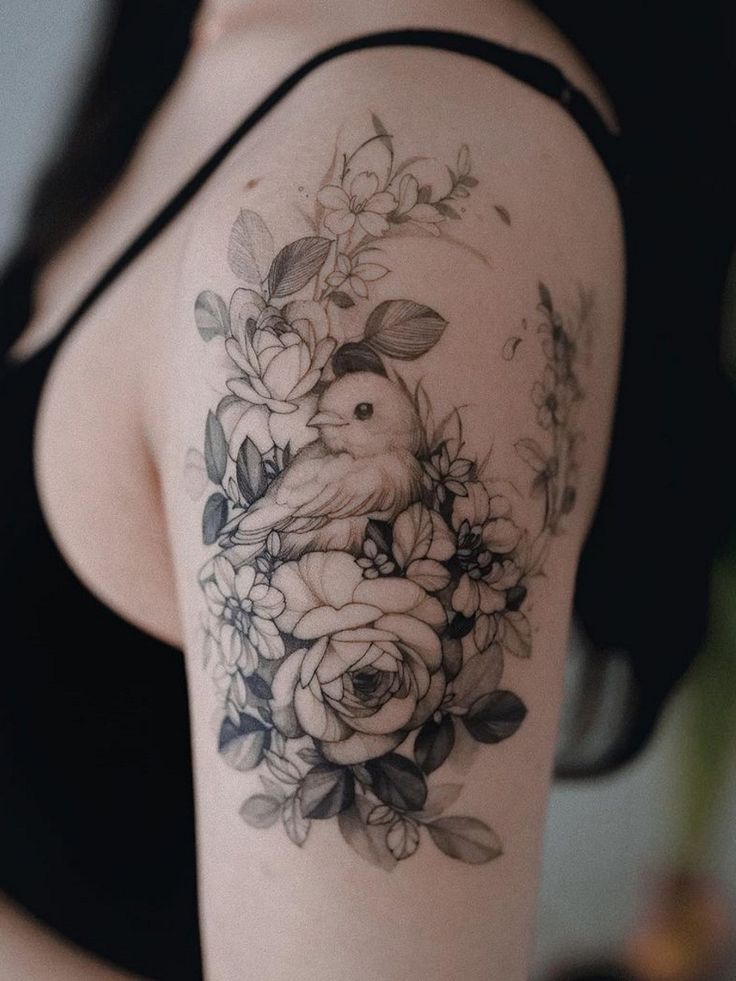 a woman's arm with flowers and a bird tattoo on her left shoulder,