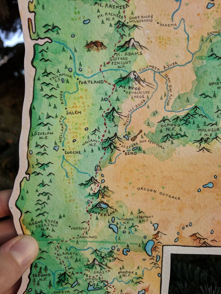 a hand holding up a map with trees and mountains in the background on a piece of paper