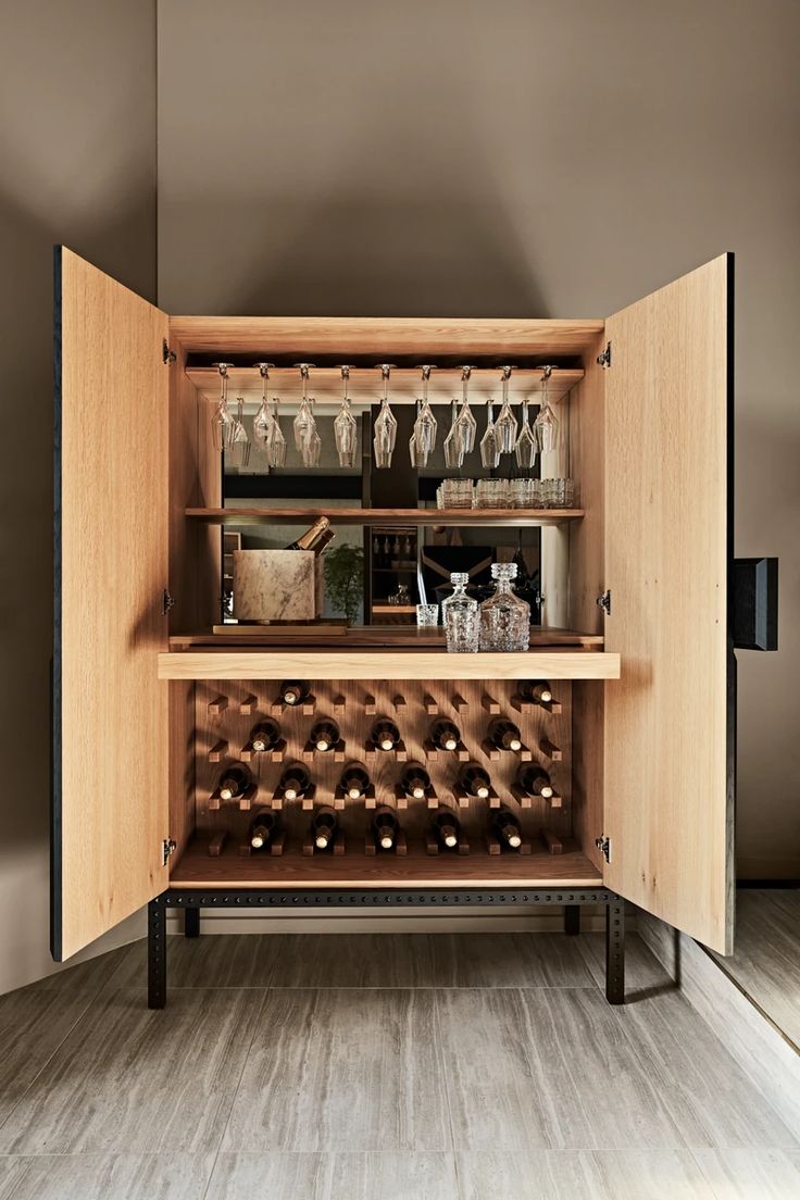 an open cabinet with many bottles and glasses on it in a room that has wood flooring