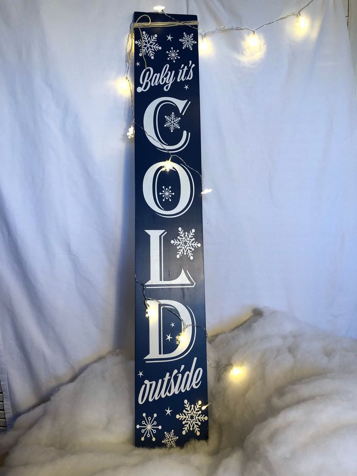 a wooden sign that says baby it's cold outside with snowflakes and lights