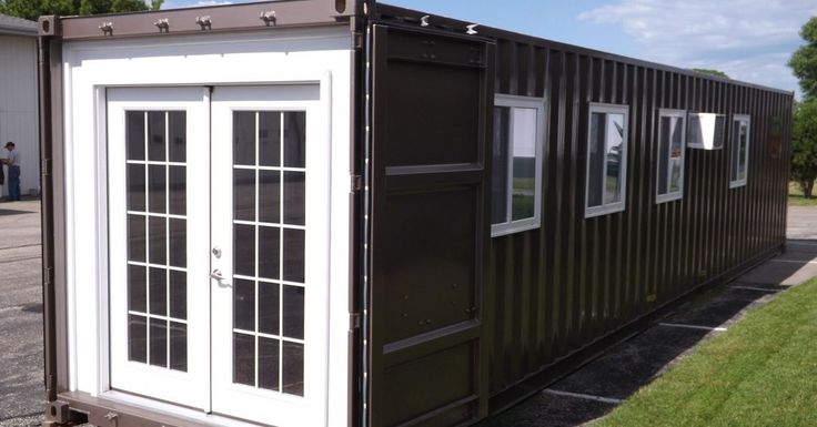 a black and white shipping container sitting on top of a grass covered field next to a building