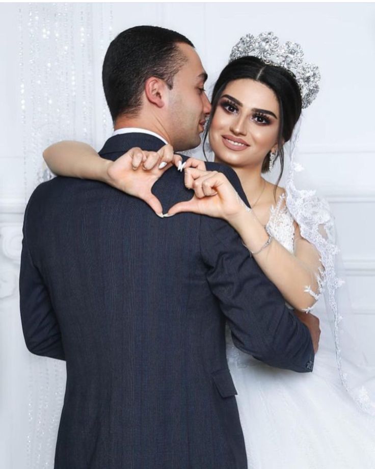 a bride and groom are making a heart shape with their hands as they pose for the camera