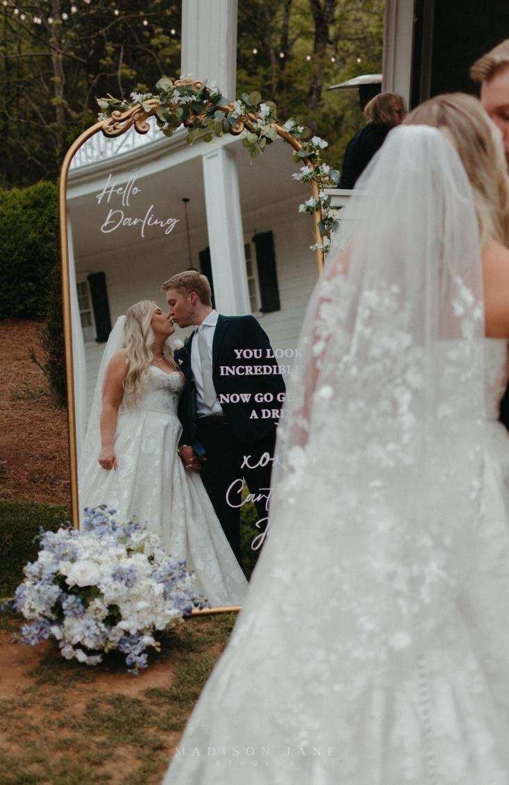 a bride and groom standing in front of a mirror with the reflection of their wedding day