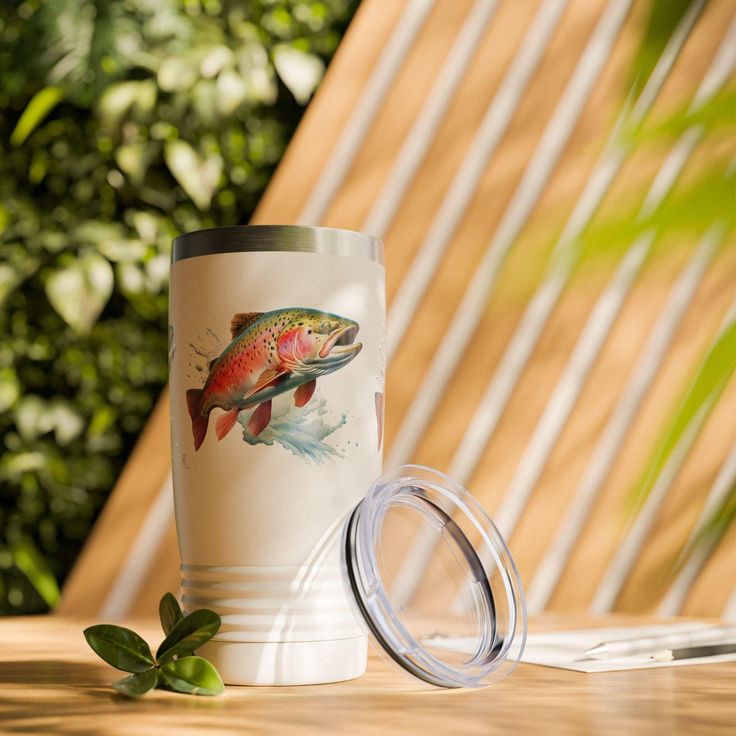 a white coffee cup with a fish on it next to a green leafy plant