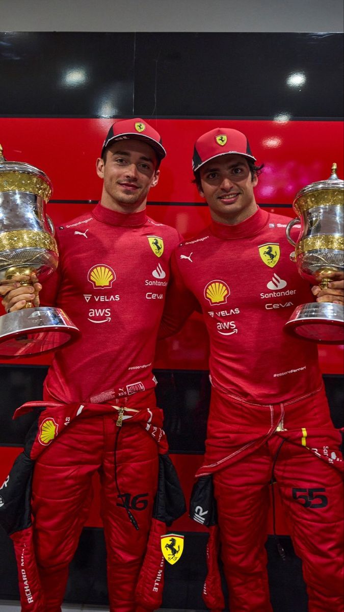 two men in red racing suits holding trophies