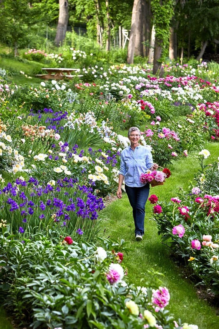 a woman walking through a lush green park filled with lots of pink and white flowers