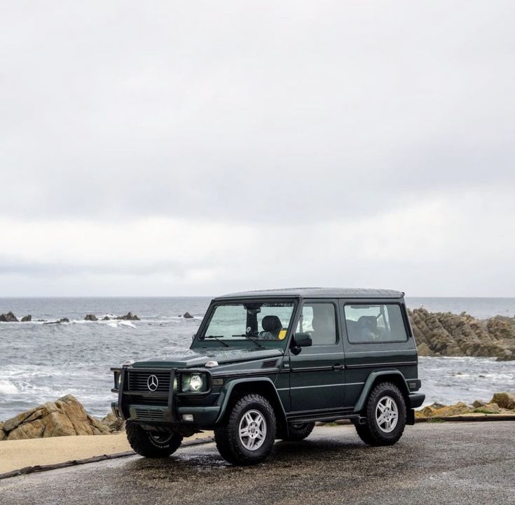 a black mercedes g class parked on the side of the road next to the ocean