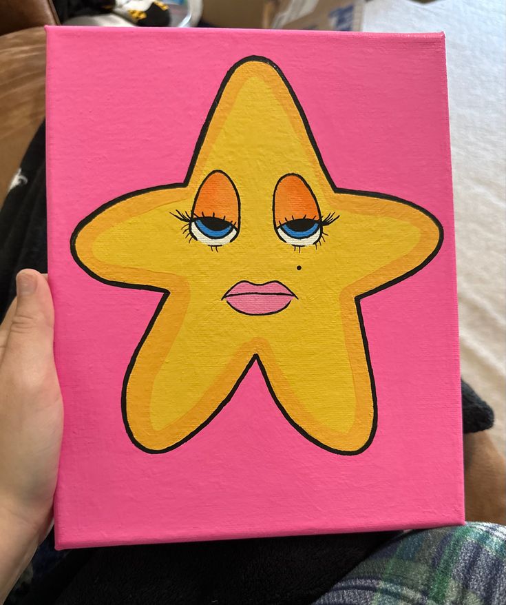 a person holding up a painting with a star on it's face and eyes