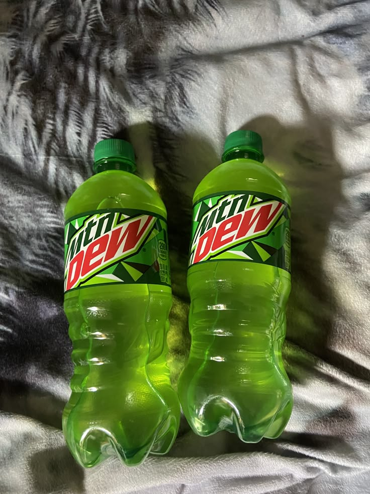 two bottles of mountain dew sitting on top of a bed