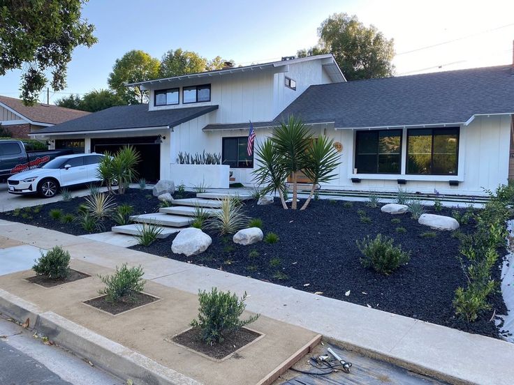 a house with landscaping in front of it and cars parked on the street behind it