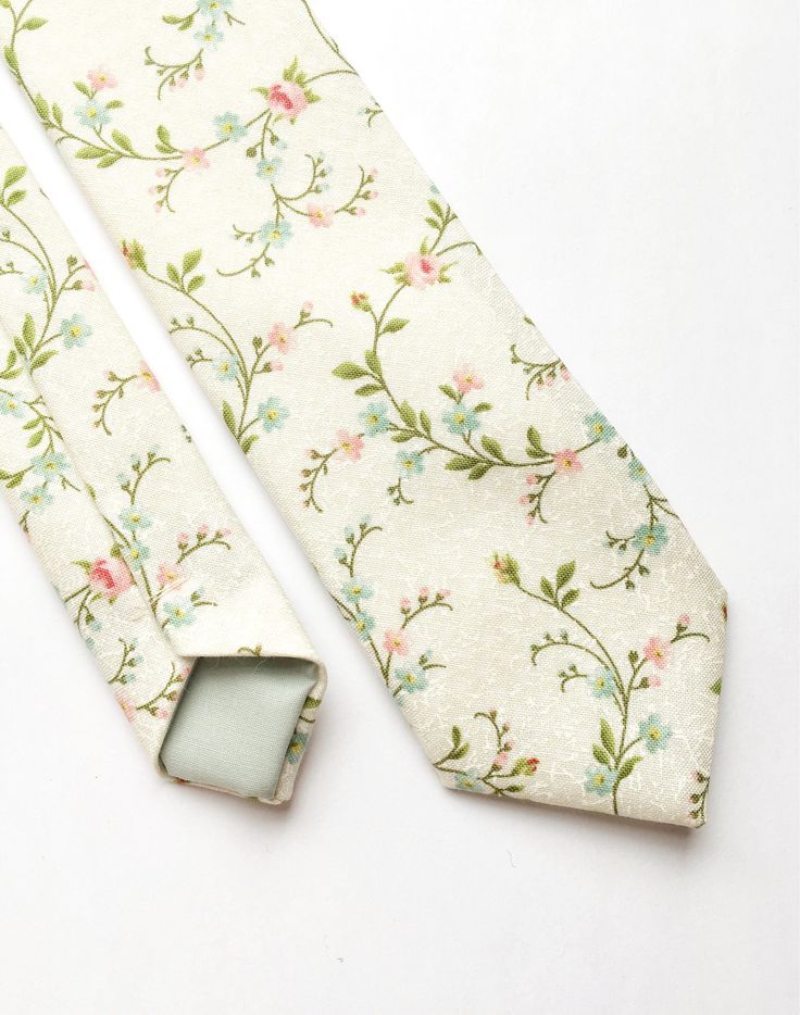 DESCRIPTION: This lovely men's skinny tie has been handmade using an ivory cotton with a pink and green floral print.  FABRIC: Cotton. LINING FABRIC: Cotton. -------------------------------------------------------------------------------------------- DETAILS: * Made the traditional way with fabric cut on the bias * Each tie has canvas lining throughout * Fabric lining just at the tip on each end of the tie * Width at the widest part measures approx 2.5 inches * The length of each tie is approx 5 Elegant Cotton Suit And Tie Accessories For Summer, Elegant Cotton Ties For Spring, Elegant Green Ties For Spring, Elegant Green Tie For Spring, Elegant Green Spring Ties, Spring Black Tie Event Ties, Spring Suit And Tie Accessories For Black Tie Events, Elegant Green Suit And Tie Accessories For Spring, Elegant Cotton Ties For Gifts