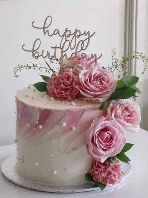 a birthday cake decorated with pink flowers and greenery