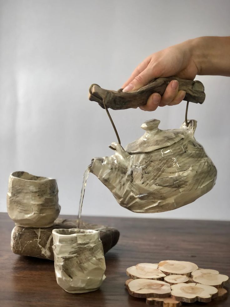 a person pouring water from a teapot into small cups on top of wooden slices