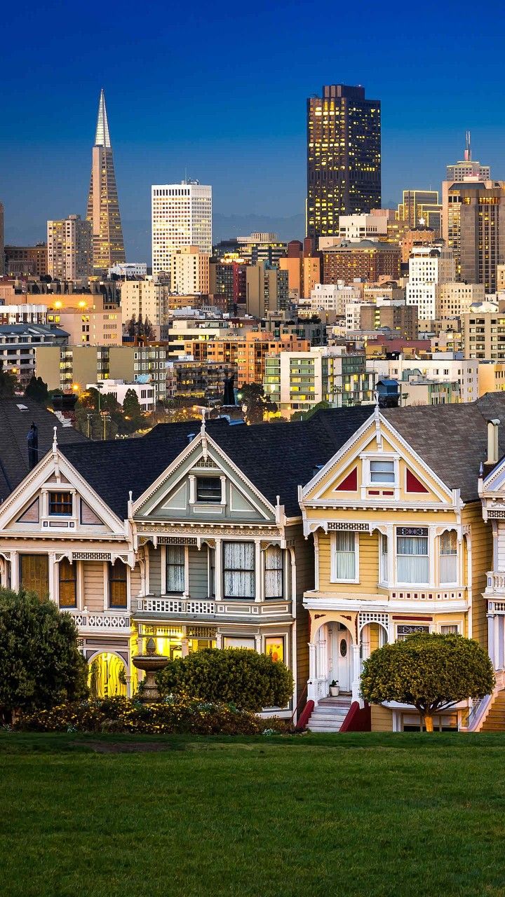 a row of houses in front of the san francisco skyline at dusk with skyscrapers in the background