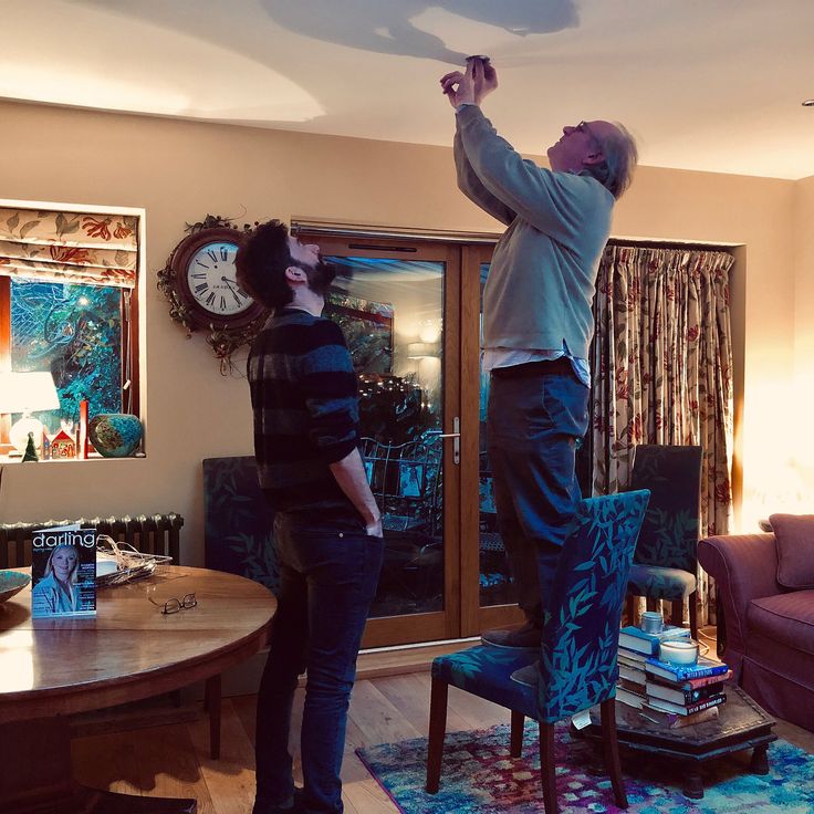 two people standing in a living room playing with a nintendo wii game controller on the ceiling