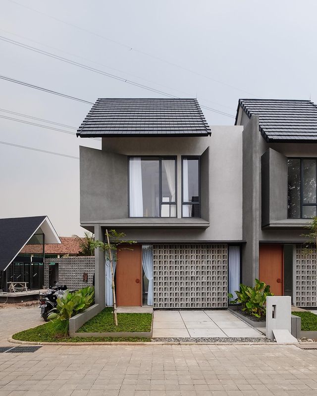 two story houses with brown doors and green plants in front of the garages on each side