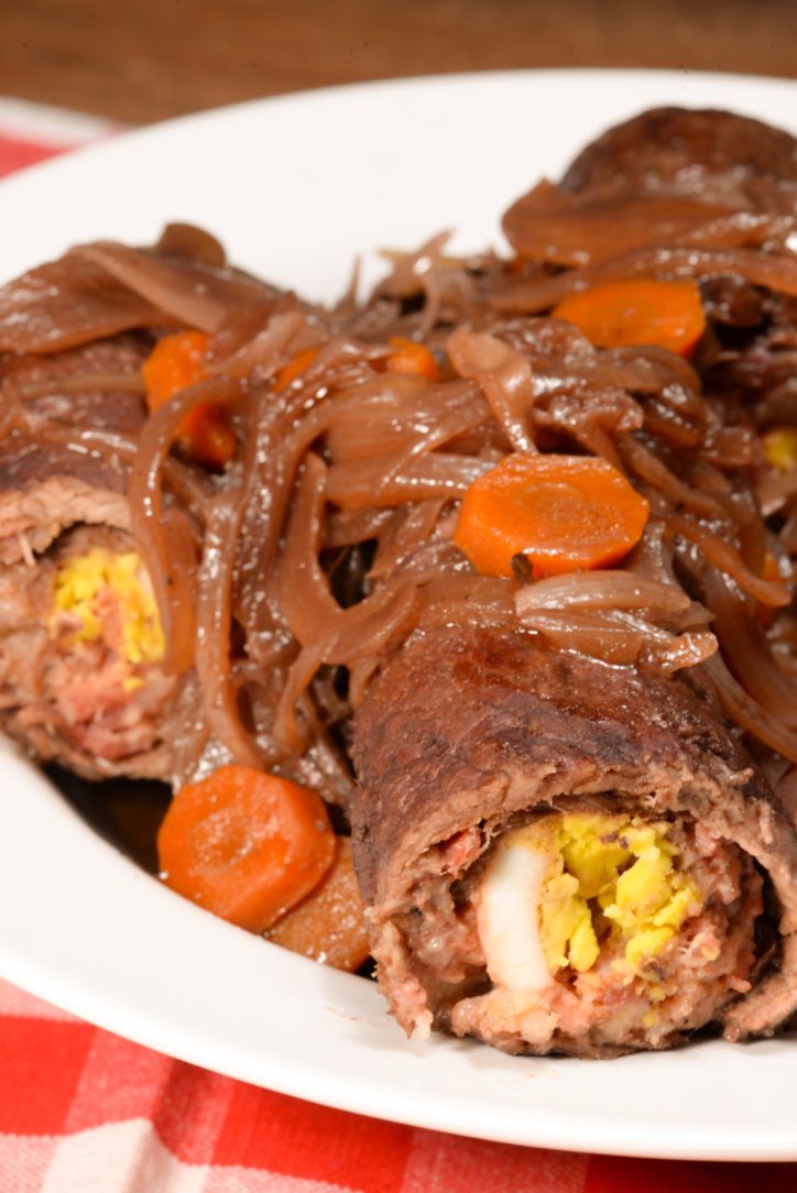 a white plate topped with meat and veggies covered in chocolate sauce on top of a checkered table cloth