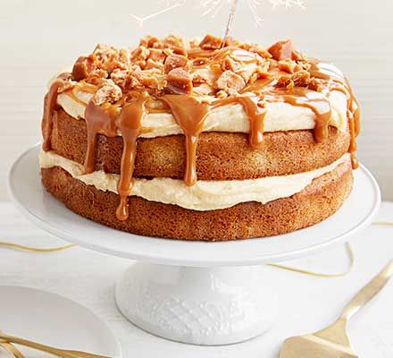 a cake with white frosting, nuts and caramel drizzle on top