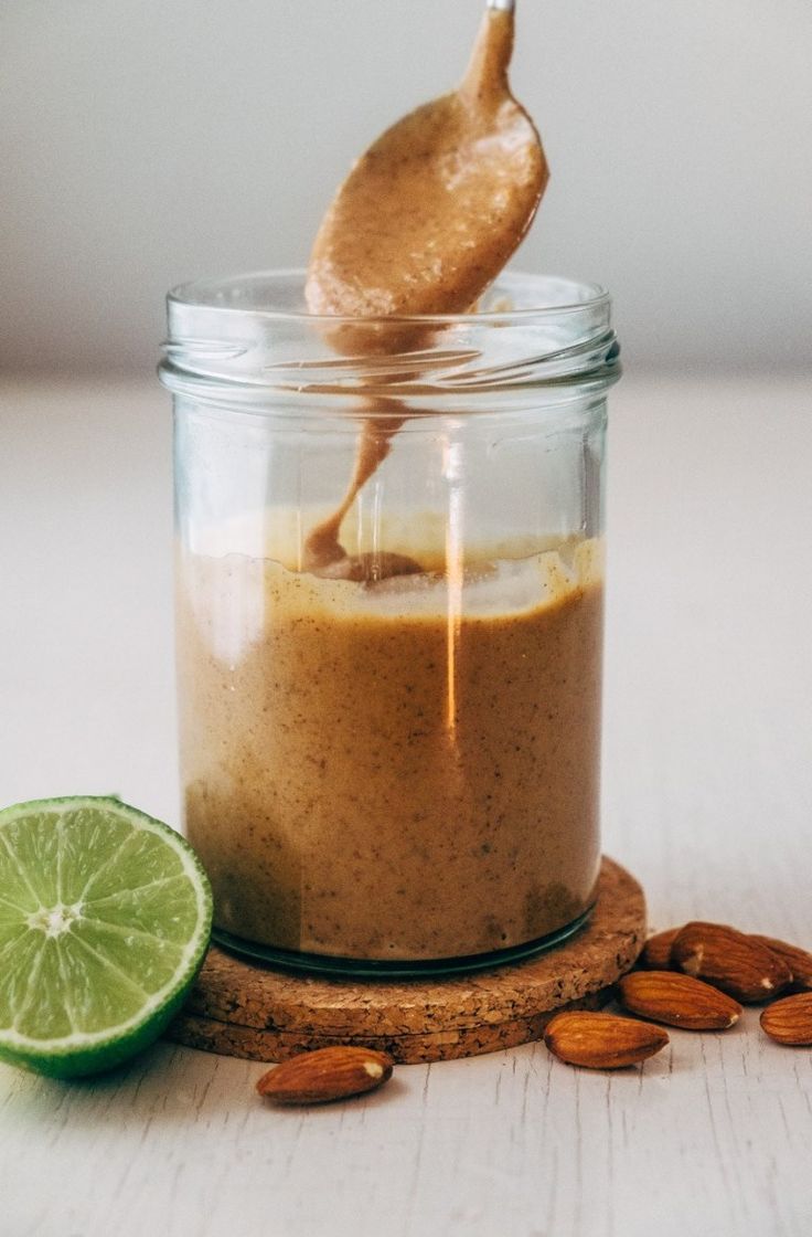 a jar filled with peanut butter and topped with a lime slice next to almonds