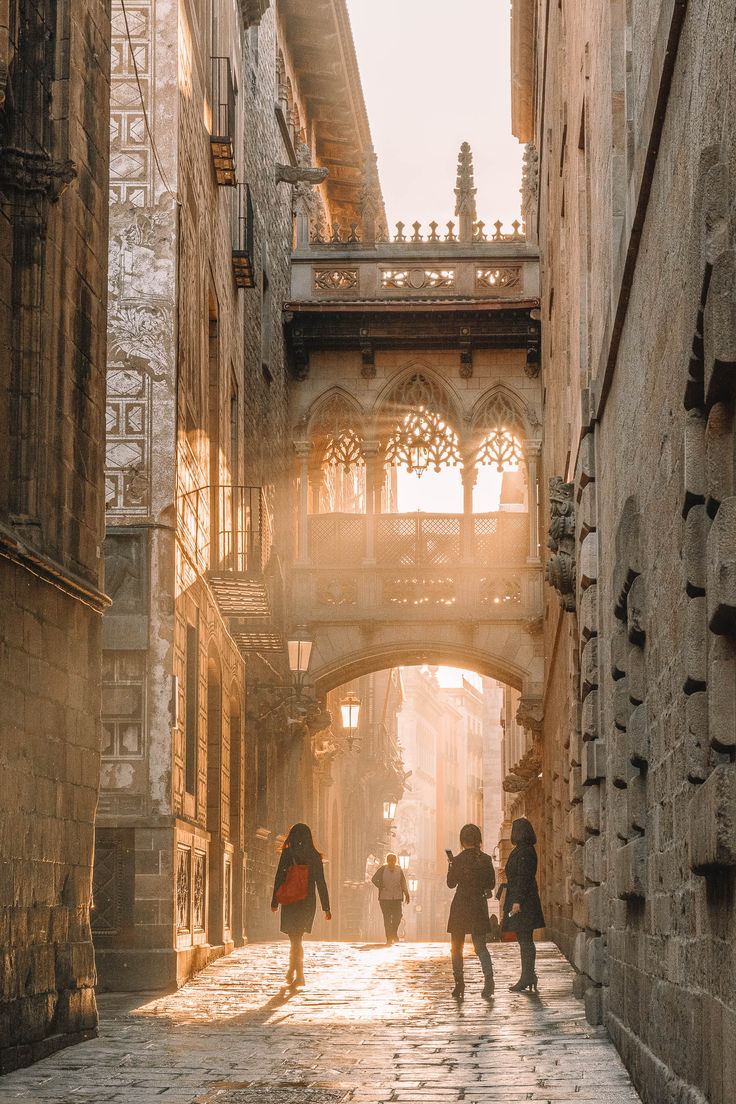 three people walking down an alley way under a bridge in the middle of some buildings