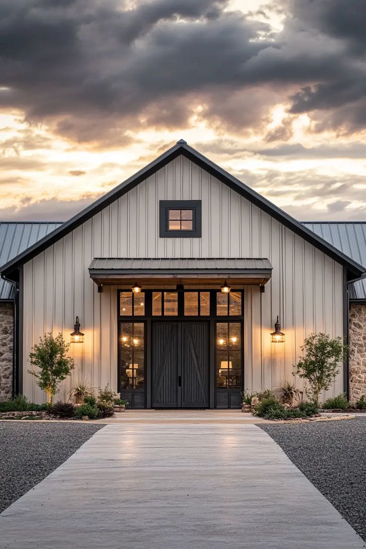 a white barn with black doors and windows under a cloudy sky in the evening light