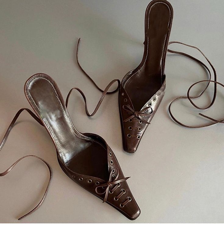 These are stylish high-heeled mules made from brown leather. The design features a pointed toe with lace-up detailing that resembles a butterfly bow, adding a touch of elegance and femininity. The heels have a sleek and glossy finish, enhancing their sophisticated look. They are perfect for both casual and formal occasions, providing a chic and versatile option for various outfits. The leather material ensures durability and comfort, making these heels a practical yet fashionable choice. Details Pointed Toe Bow Mules For Party, Party Mules With Bow And Pointed Toe, Party Bow Mules With Pointed Toe, Summer Office Lace-up Heels, Brown Mules For Party In Spring, Brown Pointed Toe Mules With Wrapped Heel, Brown Mules For Spring Party, Chic Brown Pointed Toe Mules, Brown Party Mules For Spring