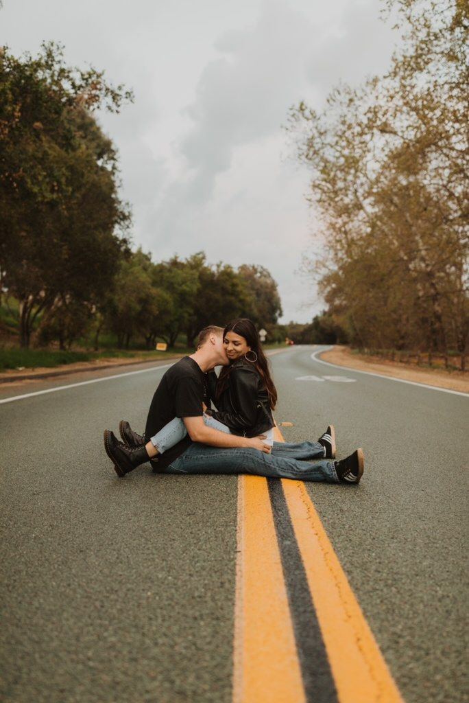 Couple sitting together in the street no one around, raining, green foliage all sides, he’s kissing her cheek they have arms and legs wrapped around each other. Pure love. Rainy Photoshoot, Rainy Day Photos, Couples Beach Photography, Couple Shoots, Road Photography, Couple Picture Poses, Engagement Photo Poses, Couple Photoshoot Poses, Night Photos