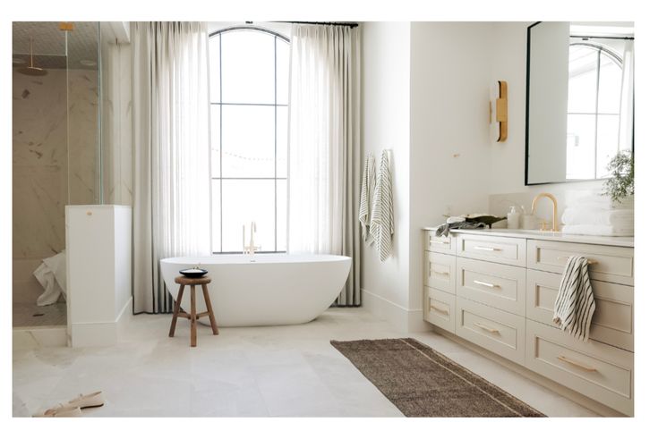 a white bath tub sitting in a bathroom next to a large window with curtains on it