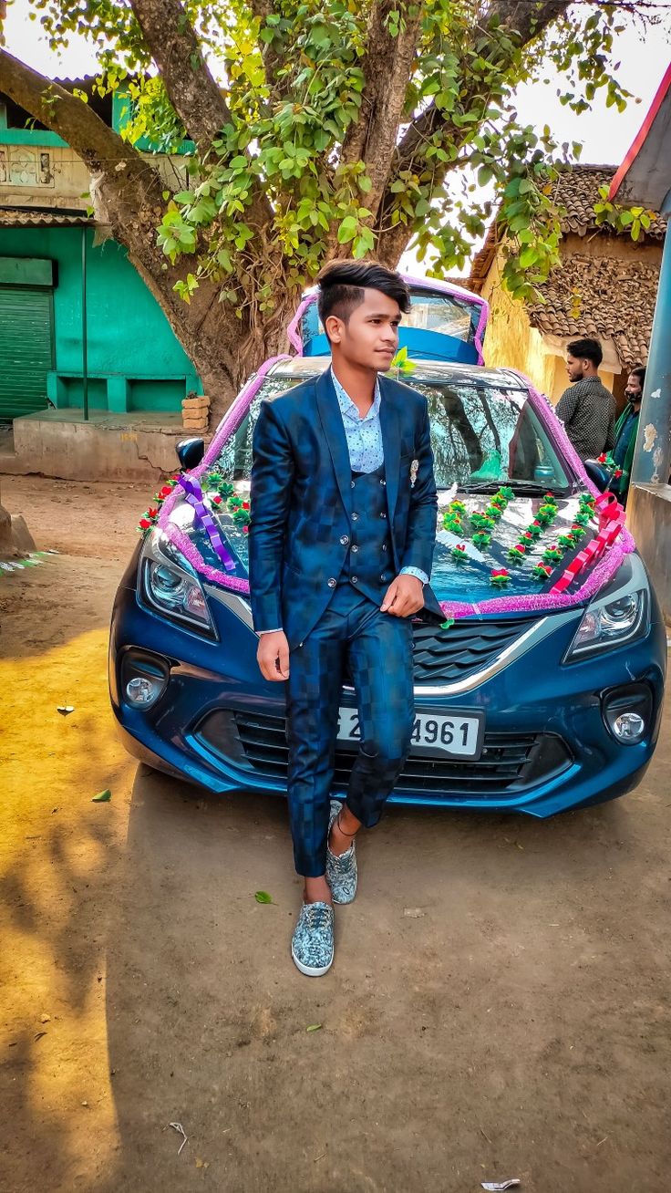 a man sitting on the hood of a blue car in front of a green tree