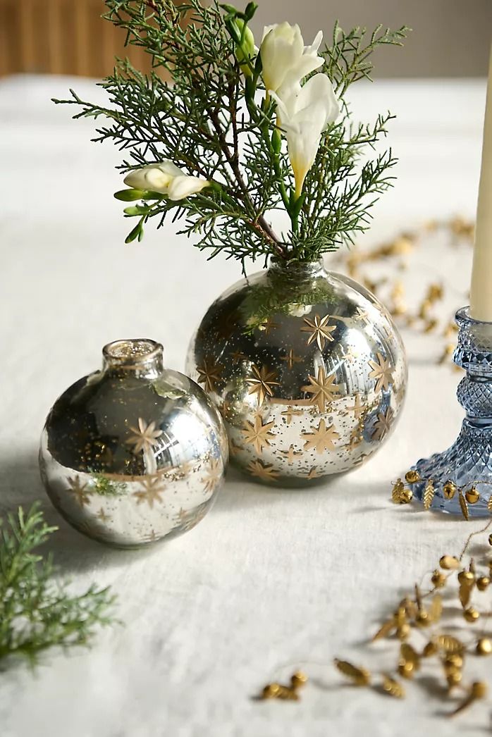 two vases with flowers in them sitting on a table next to a lit candle