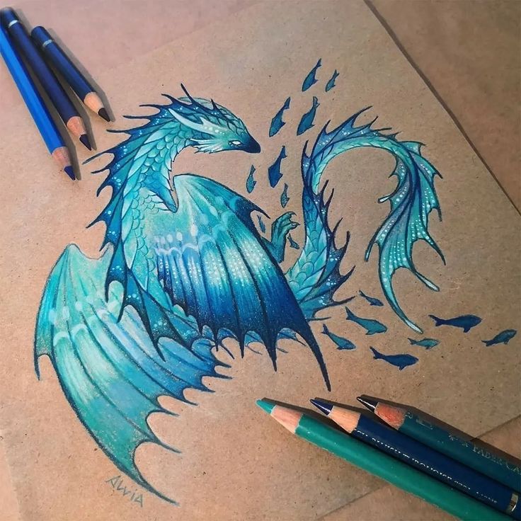 a drawing of a blue dragon sitting on top of a piece of paper next to two pencils