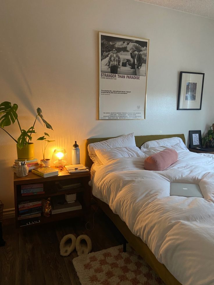 a bed with white sheets and pillows in a bedroom next to a lamp on a table