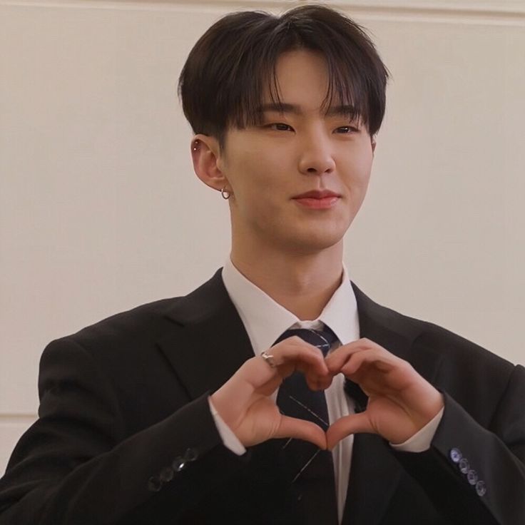 a young man in a suit making a heart with his hands while wearing a tie