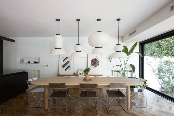 a dining room table with chairs and lights hanging from it's ceiling, in front of a large window