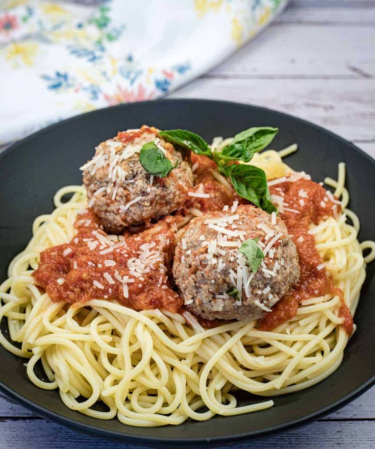 spaghetti with meatballs and sauce in a black plate on a wooden table next to a napkin