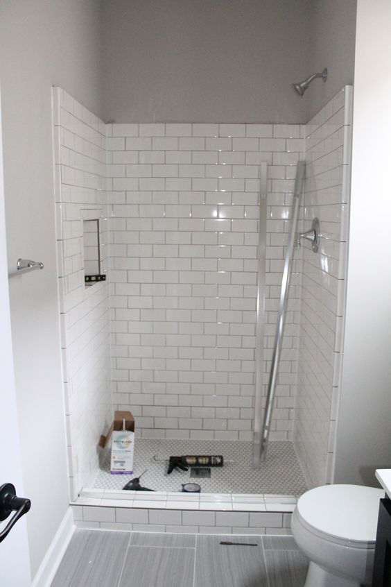 a white tiled bathroom with a toilet and shower