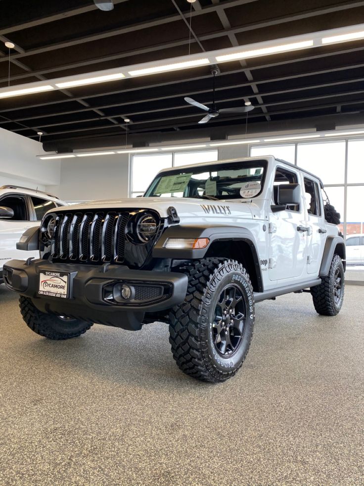 two white jeeps are parked in a showroom with large windows and black tires