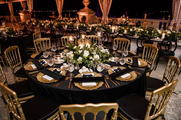 a table set up for an event with black linens and gold chairs