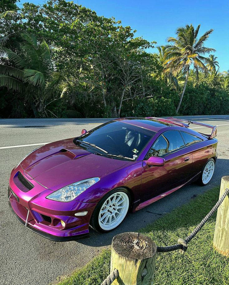 a purple sports car parked on the side of the road next to a wooden post